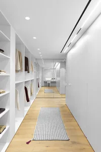 A modern white closet with white cabinets, wooden flooring, and a gray rug.