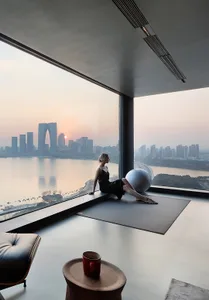 Person exercising on a workout mat in a modern room with concrete flooring, overlooking a city skyline.