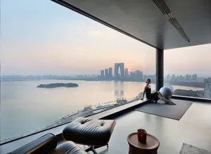 A modern living room overlooking a cityscape through a large glass window at sunset.