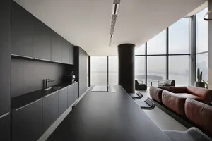 Modern, minimalist kitchen with black countertops and metal accents, glass cabinets, and a view of the cityscape outside thro