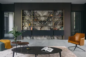 A modern living room featuring a marble wall with decorative objects and a mix of black furniture and a brown leather armchai