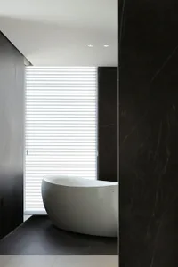 Modern bathroom with white freestanding bathtub against black marble wall and floor.