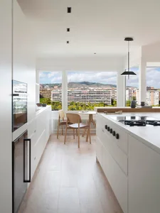 A modern kitchen with white cabinets, a gas stove, and a table overlooking the cityscape.