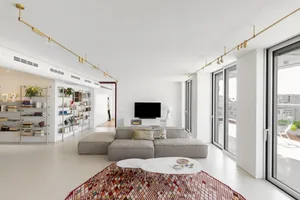 Light-colored modern interior living room with a sectional sofa, coffee table, bookshelf, and flat-screen TV.
