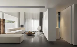 A minimalist living room with white furniture, concrete floor, and large windows.