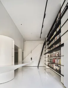 A modern library with a stairway leading to upper levels, featuring black metal shelves holding numerous books.