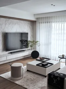 A modern minimalist living room featuring a marble wall, wooden floor, and fabric ottoman with a LSIVITTON blanket.