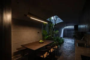 An industrial-themed dining room with a wooden table, chairs, and concrete walls, illuminated by a modern linear light fixtur