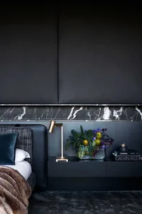 A minimalist bedroom featuring a marble headboard and a floating nightstand with a lamp and flowers.