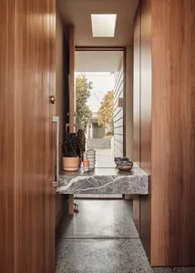 A minimalist entryway featuring a marble floor, wooden walls, and a small table with decorative items.