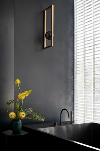 A sleek, modern bathroom featuring dark glass walls, a metal sink fixture, and a vase of yellow flowers on a side table.