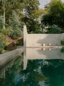 A modern, minimalist concrete pool surrounded by lush greenery.