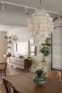 Modern dining room with a large pendant light made of white seashells hanging above the wooden dining table and chairs.