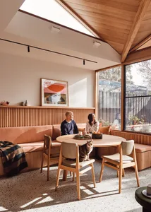 A modern dining room features a wooden table, wooden chairs, a wooden bench, a terrazzo floor, and a cat sitting on one of th