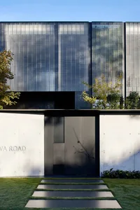 A modern house exterior with concrete walls, a large glass window, and a garden pathway.