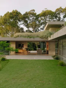 Modern house exterior with concrete and terrazzo materials, featuring a green roof and large glass windows.