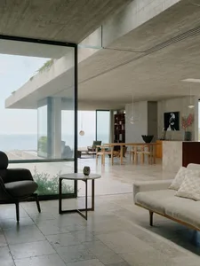 Modern residential living room featuring concrete walls and glass windows overlooking the ocean.