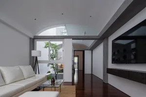 Photograph of a modern living room featuring a white couch, glass table, and concrete flooring.