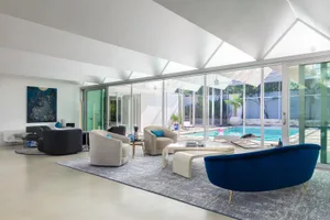 A modern living room featuring glass furniture and a large glass wall with a view of a pool.