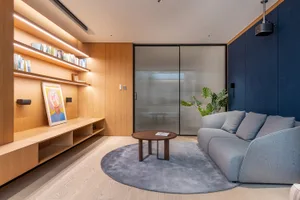 A modern living room with a wooden floor, glass door, and a grey sofa on a circular rug, illuminated by soft lighting.
