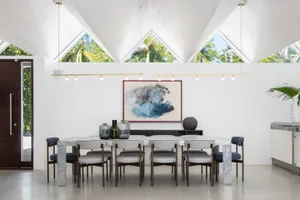 A modern dining room with a marble dining table surrounded by upholstered chairs, framed abstract art on the wall, and large 