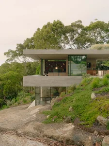 A modern minimalist cabin built into a hillside with concrete exterior and large windows.