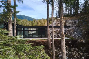 Modern residential home with large glass windows and concrete exterior nestled in a forested area.