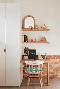 A minimalist home office setup featuring a wooden desk, a white chair, and a brick wall backdrop.