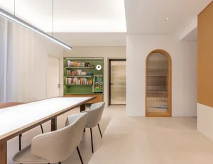 A modern dining room featuring white marble countertops and wooden chairs with a glass partition and green shelving unit.