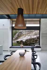 A modern dining room with a wooden table and seating area, featuring a large window with a view of rocks and nature outside.