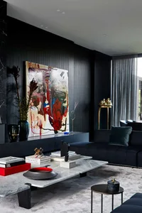 A modern living room featuring a concrete coffee table with leather seating, brass accents, and a large abstract painting.