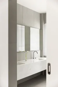 A minimalist bathroom featuring a white marble sink and countertop, with a large mirror and sleek faucet.