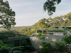 A modern residential exterior with concrete and glass materials and lush greenery.