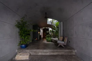 A minimalist entrance with concrete walls and a natural stone step leading to a greenery-filled courtyard.