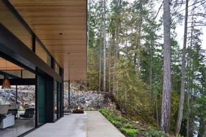 Modern residential exterior featuring wood, concrete, and stone materials in a forest setting.