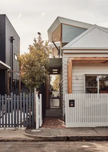 Modern house with wooden and metallic accents, featuring a white picket fence and a corrugated metal roof.
