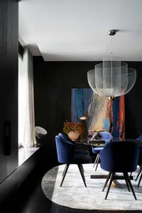 A modern interior design featuring a black wall, glass table, blue velvet chairs, and a large abstract painting.