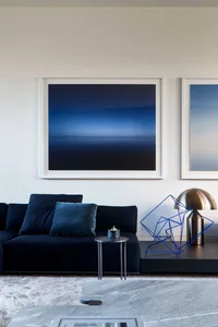 A modern interior design living room featuring a dark blue sectional sofa with plush cushions, marble coffee table, metal lam