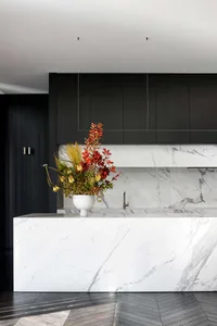 A modern kitchen with a large marble island featuring a vase of flowers and black cabinets.