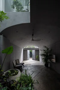 Modern indoor entrance with concrete walls and floor, plants, and natural light coming through an open door.