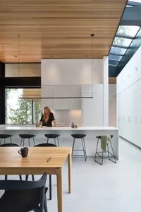 A modern kitchen with white painted cabinets, black stools, and a large skylight.