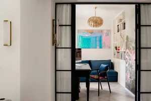 A home office with a blue sofa, wooden floor, and a gold chandelier hanging from the ceiling.