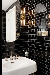 Modern black tiled bathroom with a white sink and gold accents