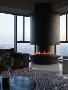 Modern living room featuring a sleek, black cylindrical fireplace made of concrete, with a comfortable sofa, a round wooden c