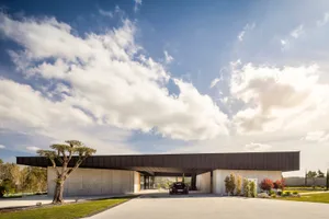 A modern house with a concrete exterior under a blue sky with white clouds.
