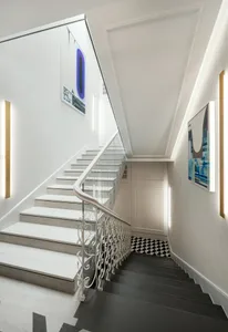 Modern interior staircase with concrete steps, white walls, and a black and white checkered floor. Features abstract art on t