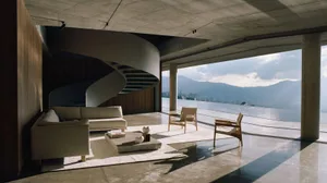 A modern living room featuring concrete walls and a glass spiral staircase overlooking mountains.