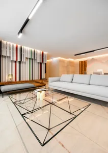 A modern living room featuring a glass and wool table, a white sofa, and geometric lines on the wall.