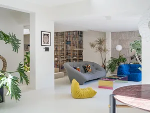 A stylish modern living room with a library area featuring a grey sofa, colorful cushions, and an extensive bookshelf.