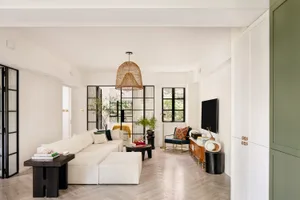 Modern living room featuring a white sectional sofa, woven pendant light, and green cabinets.